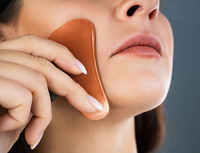 A copper gua sha tool being used on a women's face.